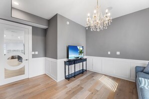 A modern living room with a flat-screen TV on a black console table, a chandelier, and a wooden floor. - Azure Bay Retreat (Ocean City)