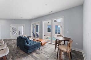 Un vaste espace de vie comprenant un canapé bleu, une table à manger en bois et des chaises, un escalier et de grandes fen êtres.