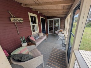 A covered porch with a wicker sofa, a small table, and a potted plant.