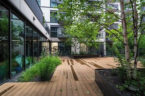 Ein modernes Gebäude mit einer Holzdielen-Terrasse, umgeben von viel Grün und Glasfenstern.