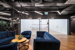 Ein modernes Interieur mit Holzboden, blau gepolsterten Stühlen, einem kleinen runden Tisch mit Pflanze und einer Glastrennwand mit roter Linie.