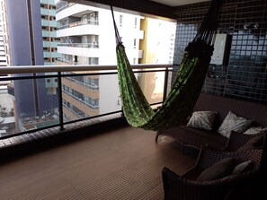 A balcony with a hammock, wicker furniture, and a view of surrounding buildings. - Landscape Apartment in Fortaleza Gold (Fortaleza)