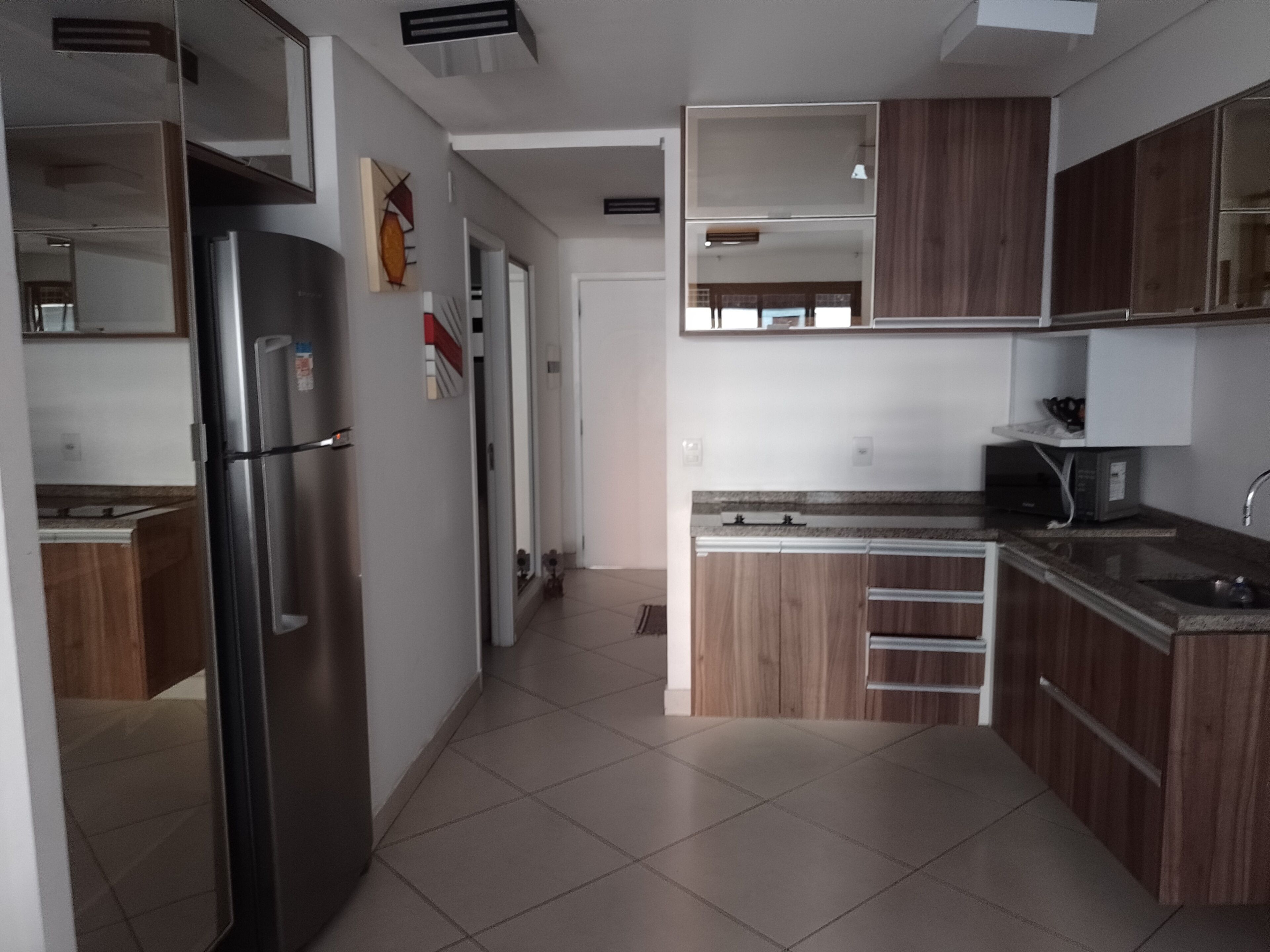 A modern kitchen with a stainless steel refrigerator, wooden cabinets, a microwave, and a sink.
