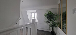Eine Treppe mit weißen Geländern führt zu einem Raum, der einen Heizkörper, ein Fenster und eine große Topfpflanze beinhaltet.