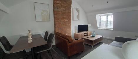 A furnished room with a dining table, a sofa, a TV, and a window.