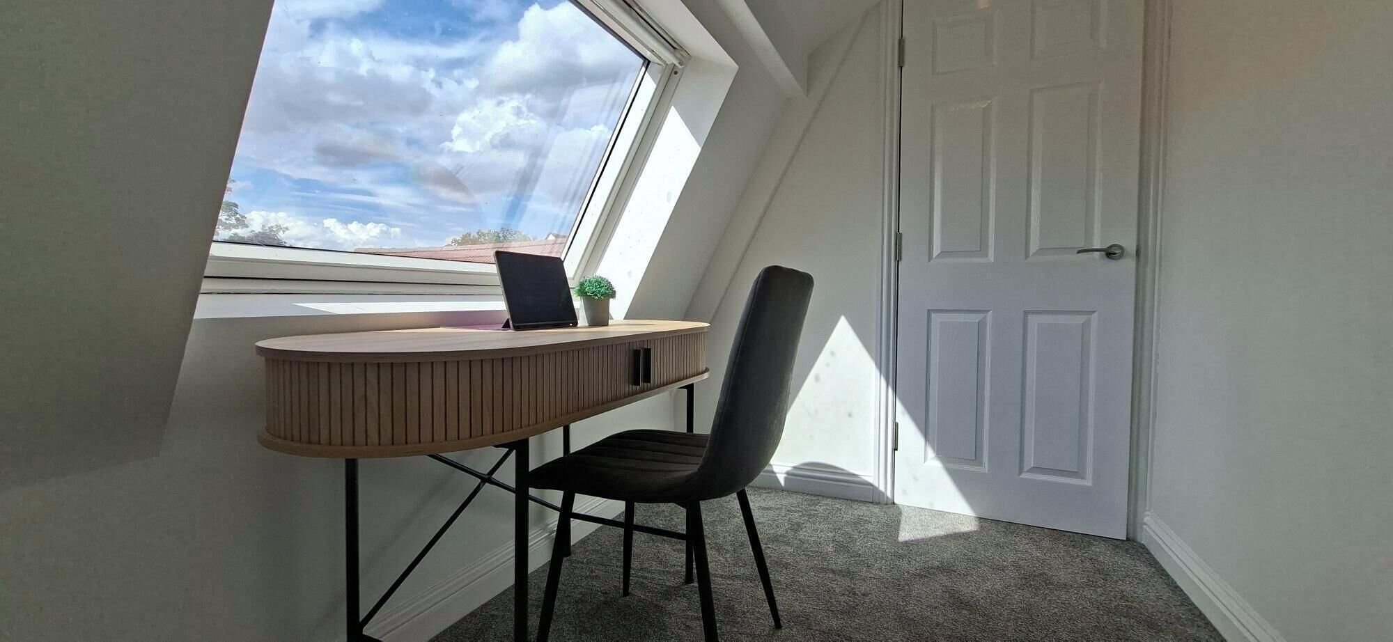 A small, private office space with a desk and chair, a potted plant, and a view through a skylight.