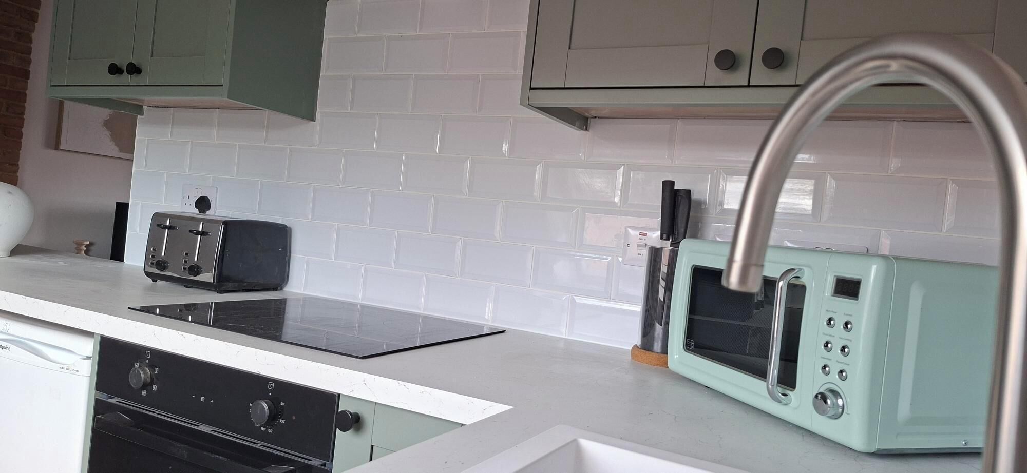 Une cuisine avec un dosseret de carreaux blancs, une plaque de cuisson à induction noire, un grille-pain bleu clair de style rétro et un robinet en acier inoxydable.