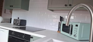 A kitchen with white tiled backsplash, a black induction cooktop, a light blue retro-style toaster, and a stainless steel faucet.