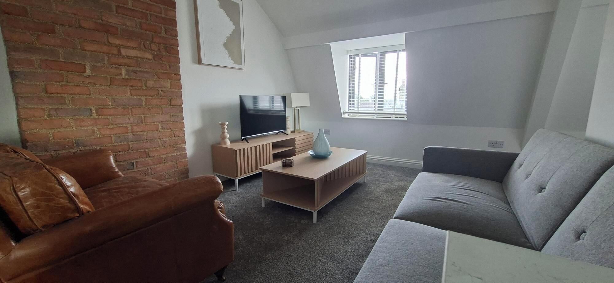 A living room with a brick wall, a television, a sofa, and a window.
