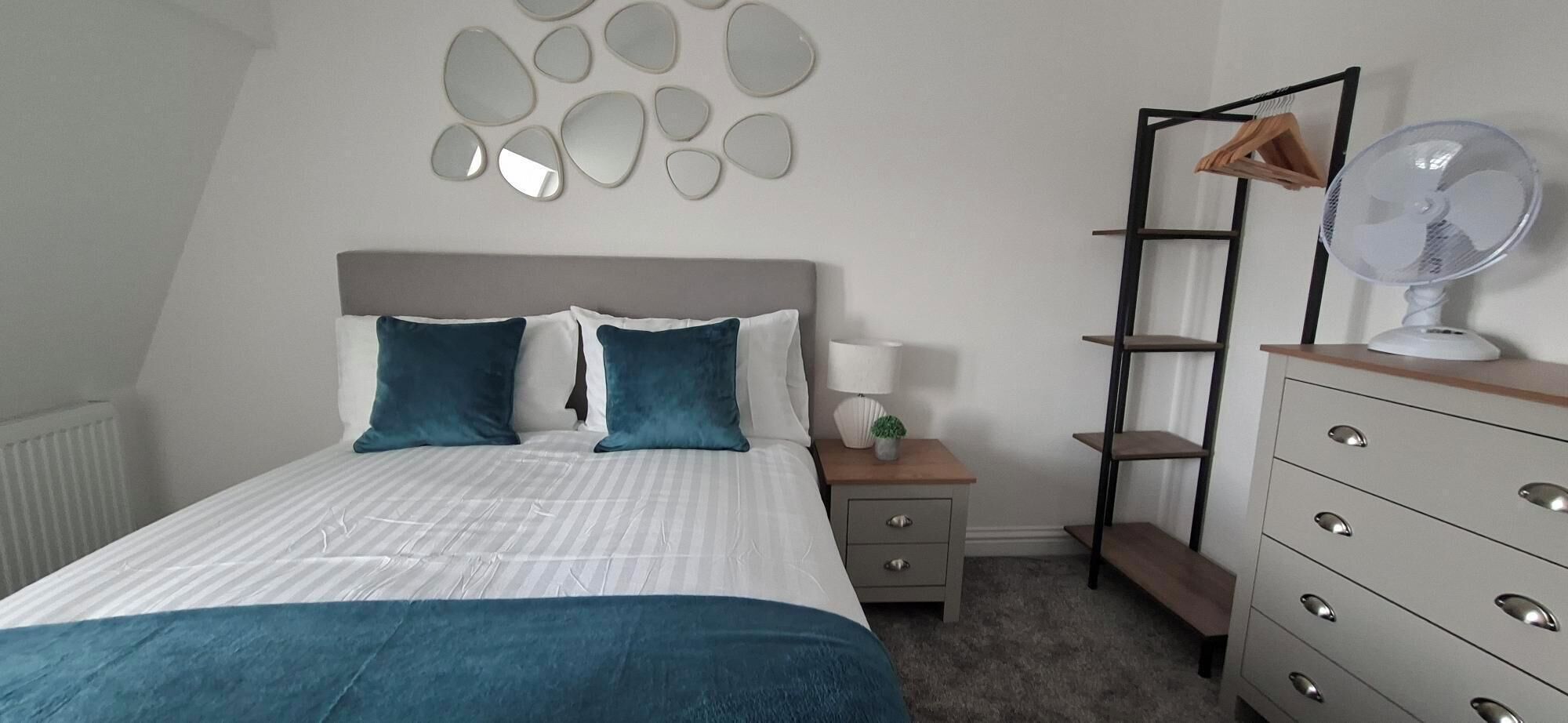 A bedroom with a bed, bedside table, lamp, and a dresser with drawers.