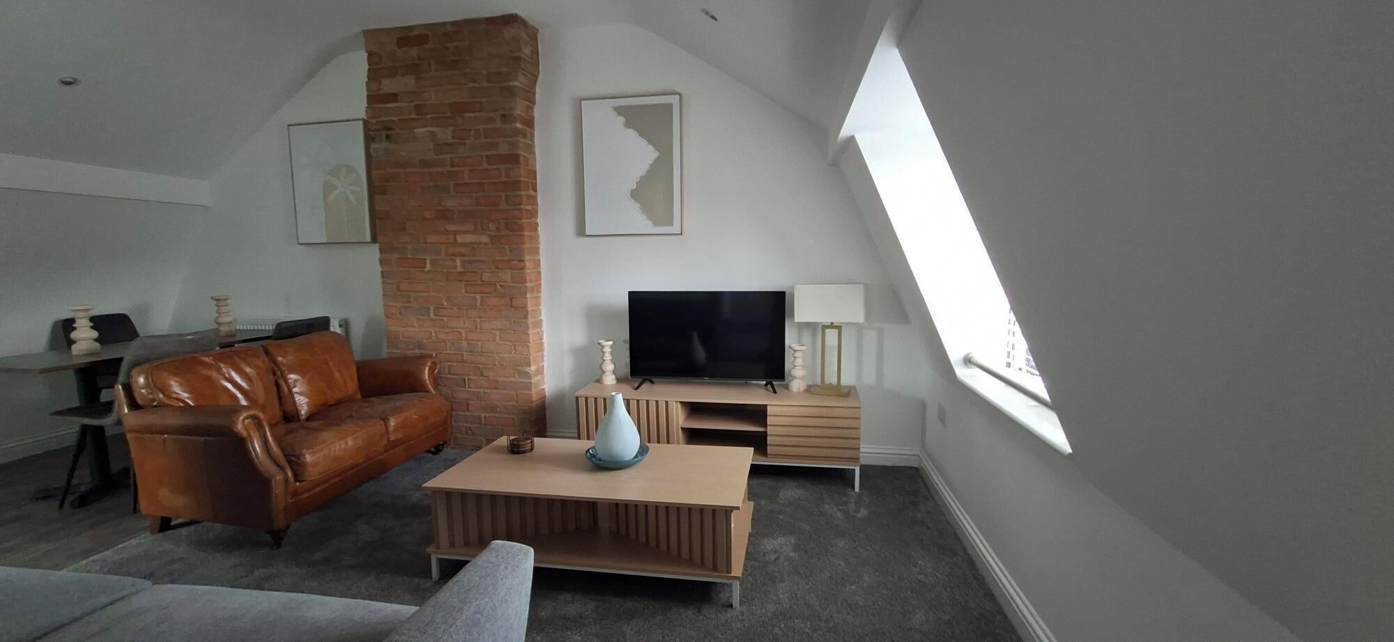 Ein Loft-Wohnzimmer mit Kamin aus Backstein, einem Ledersofa, einem Flachbildfernseher und einem großen Oberlicht.