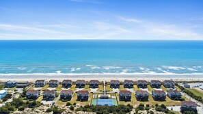 Zona residencial costeira com imóveis na orla, quadra de tênis e vista clara do oceano.