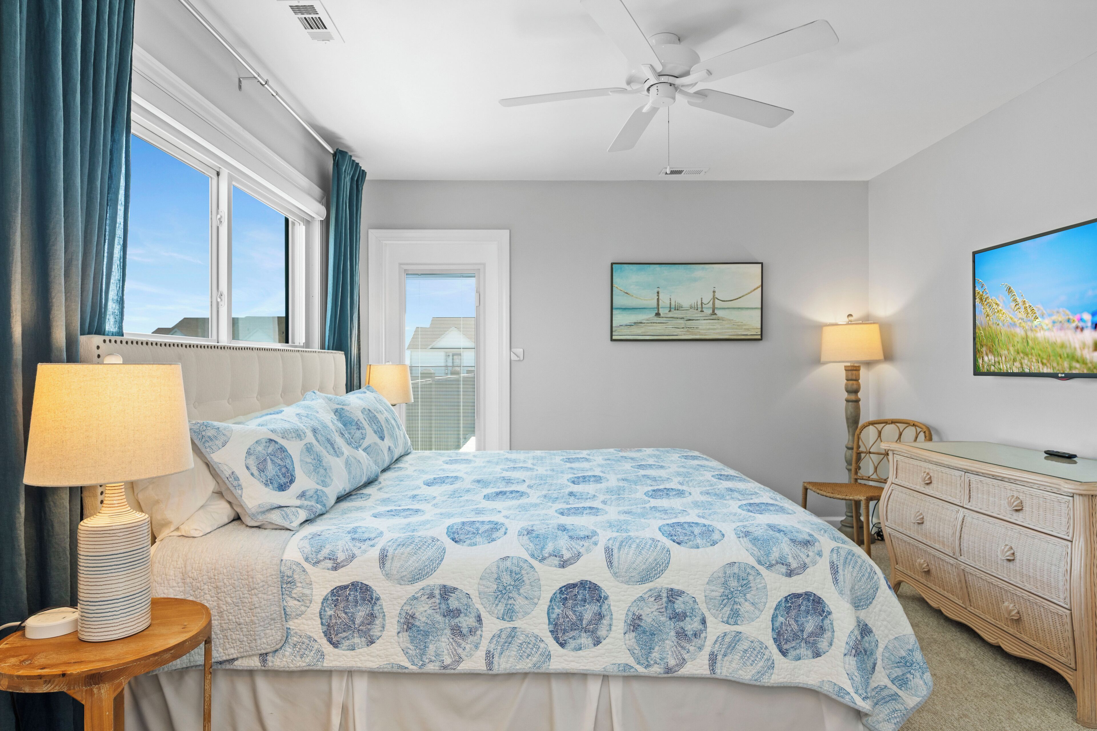 A bedroom with a bed, a ceiling fan, a painting, a lamp, and a dresser.