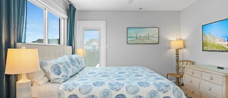A bedroom with a bed, a ceiling fan, a painting, a lamp, and a dresser.