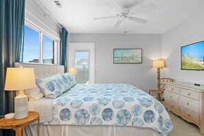 Ein Schlafzimmer mit einem Bett, einem Deckenventilator, einem Gemälde, einer Lampe und einem Schminktisch.