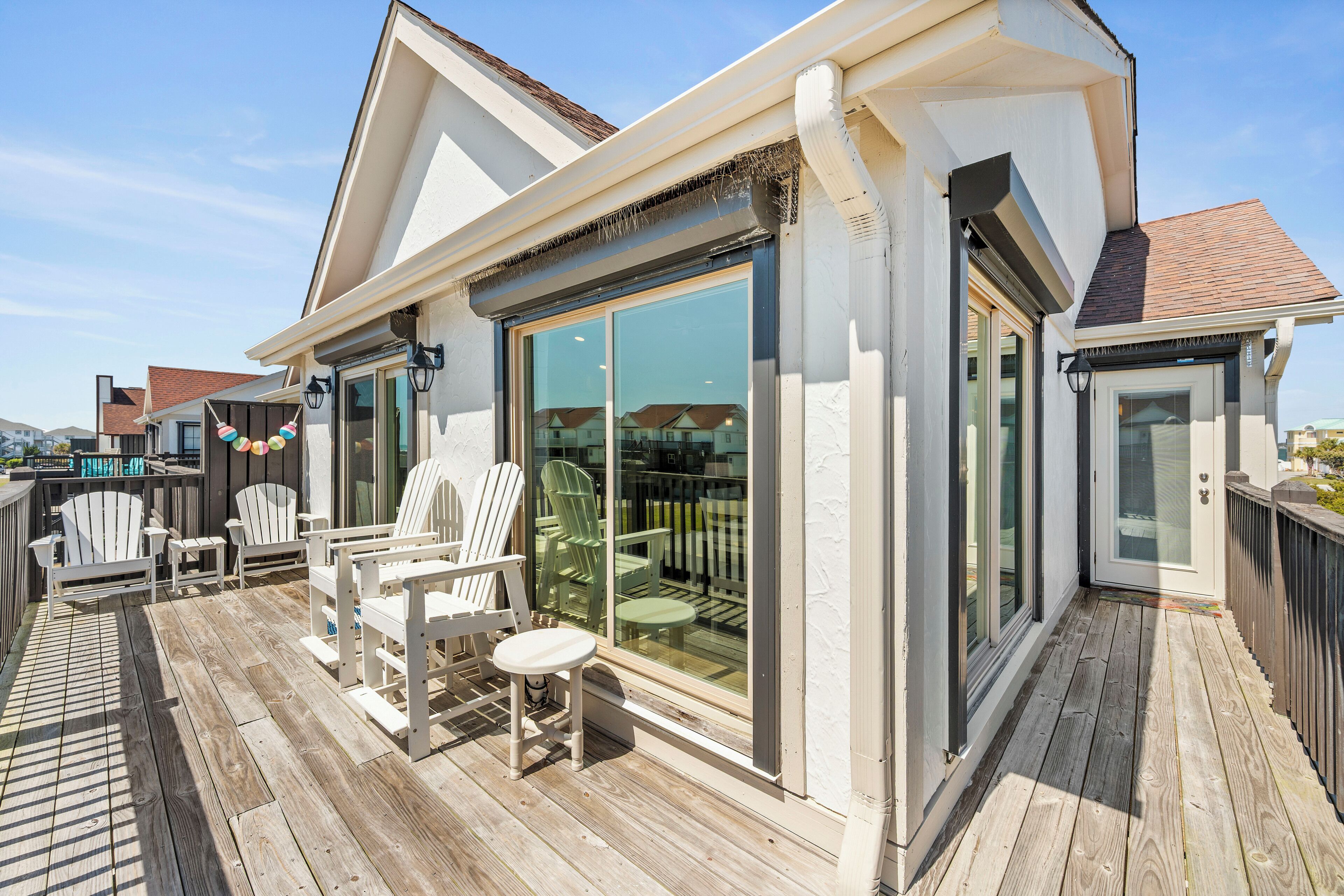 A covered outdoor deck with Adirondack chairs and a dining table, overlooking a residential area.