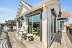 A covered outdoor deck with Adirondack chairs and a dining table, overlooking a residential area. - Top-Floor Ocean Views | Pool + Beach Access (Emerald Isle)