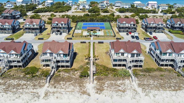 Een kustwoongebied met huizen aan het strand, voorzien van balkons, een tennisbaan en een zandstrand.