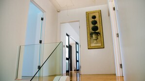 Eine Treppe mit Glasgeländern führt zu einer Zwischenebene. Über der Zwischenebene hängt ein gerahmtes Kunstwerk.