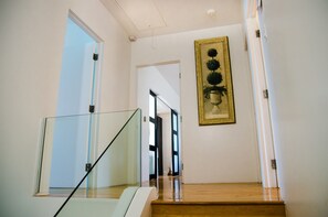Eine Treppe mit Glasgeländern führt zu einer Zwischenebene. Über der Zwischenebene hängt ein gerahmtes Kunstwerk.