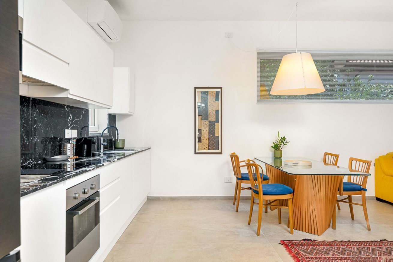 Ett modernt kök med matplats, utrustat med en bänkskiva i marmor, rostfria vitvaror och ett matbord i trä med tillhörande stolar.