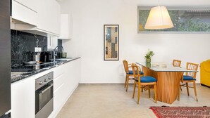 Moderni keittiö, jossa on ruokailutila. Keittiössä on marmoritaso, ruostumattomasta teräksestä valmistetut kodinkoneet sekä puinen ruokapöytä tuoleineen.