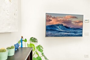 Eine Wand mit einem gerahmten Bild von einer Welle, einer kleinen Figur und einem Blumentopf.
