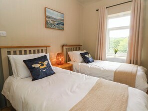 A bedroom with two beds, a bedside lamp, a painting on the wall, and a window with curtains. - 2 Bentley Bridge Cottages (Matlock)