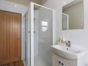 A bathroom with a wooden door, a glass shower enclosure, a white sink with a mirror above it, and toiletries on the sink. - 2 Bentley Bridge Cottages (Matlock)