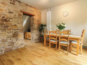 A dining area with a stone wall, wooden table, chairs, a clock, and a potted plant. - 2 Bentley Bridge Cottages (Matlock)