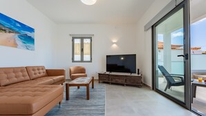 A living room with a sofa, armchair, TV, and a glass door leading to an outdoor area. - Casa Turalves - By WeHostMadeira (Porto Santo)