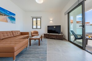 A living room with a sofa, armchair, TV, and a glass door leading to an outdoor area.