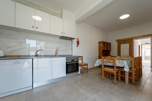 A modern kitchen with white cabinets, a built-in oven, and a dining area with wooden chairs and a table.