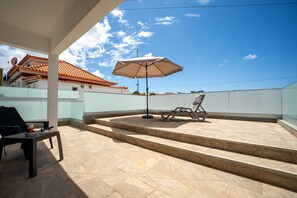 A rooftop terrace with a table, a chair, and an umbrella.