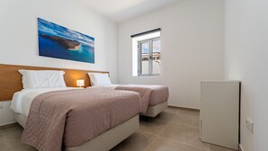 A hotel room with a bed, a bedside table with a lamp, a window with a view, and a refrigerator. - Casa Turalves - By WeHostMadeira (Porto Santo)