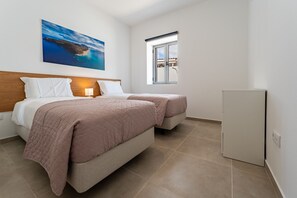A hotel room with a bed, a bedside table with a lamp, a window with a view, and a refrigerator.