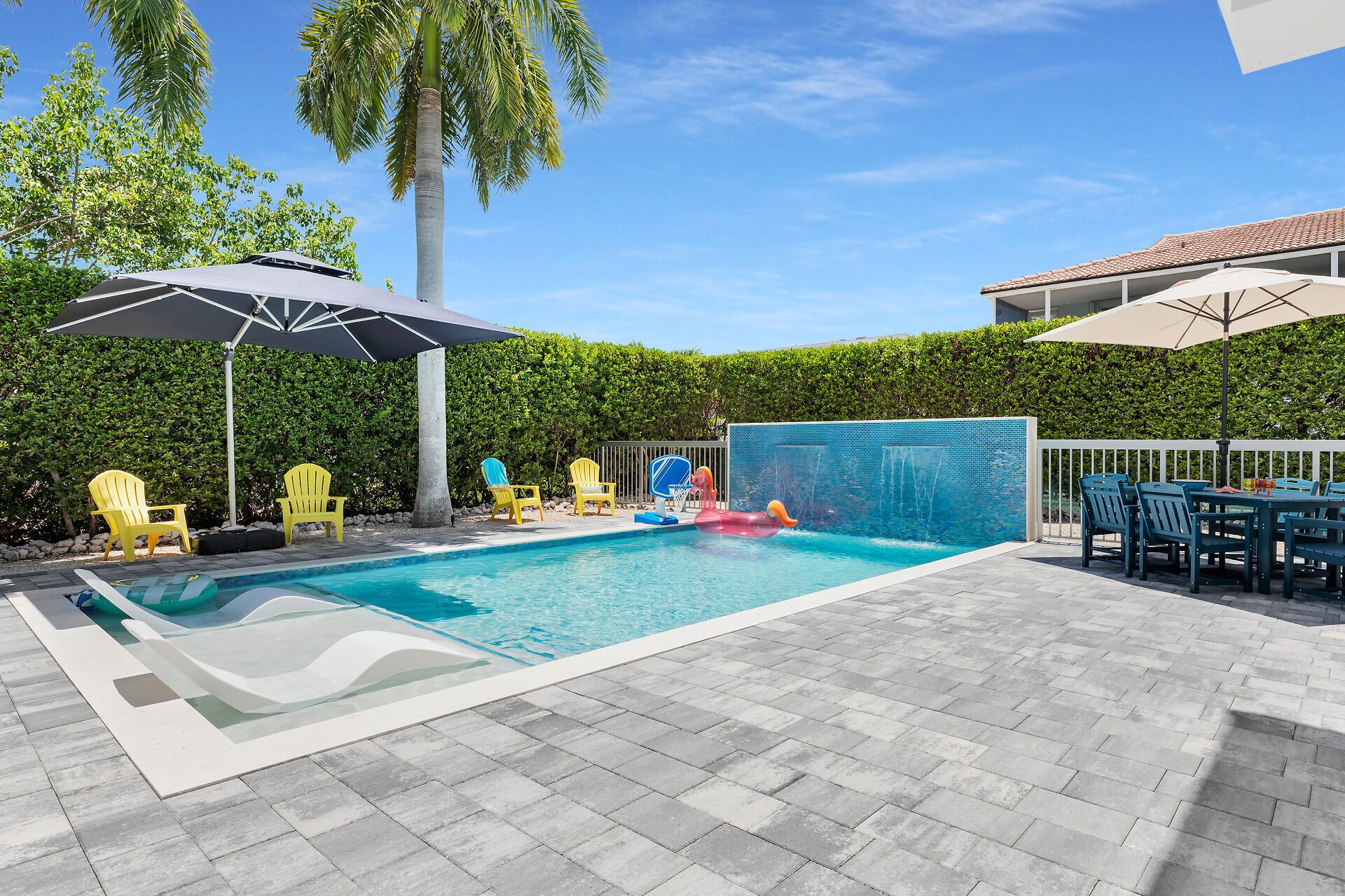A swimming pool with a small waterfall feature, surrounded by a paved deck and yellow chairs.