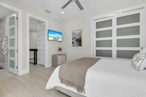 Ein Schlafzimmer mit Bett, Fernseher, einem Gemälde und einem Kleiderschrank mit Milchglasschranktüren.
