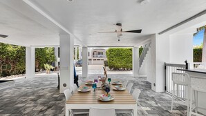 An outdoor covered patio with a wooden table set for dining, surrounded by white chairs. - Brand new, walking distance to Sombrero Beach! 4 Bed/4.5 Bath outdoor kitchen. (Marathon)