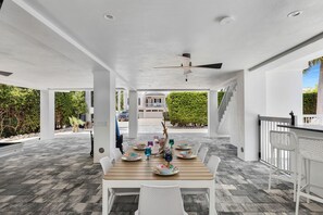 An outdoor covered patio with a wooden table set for dining, surrounded by white chairs. - Brand new, walking distance to Sombrero Beach! 4 Bed/4.5 Bath outdoor kitchen. (Marathon)