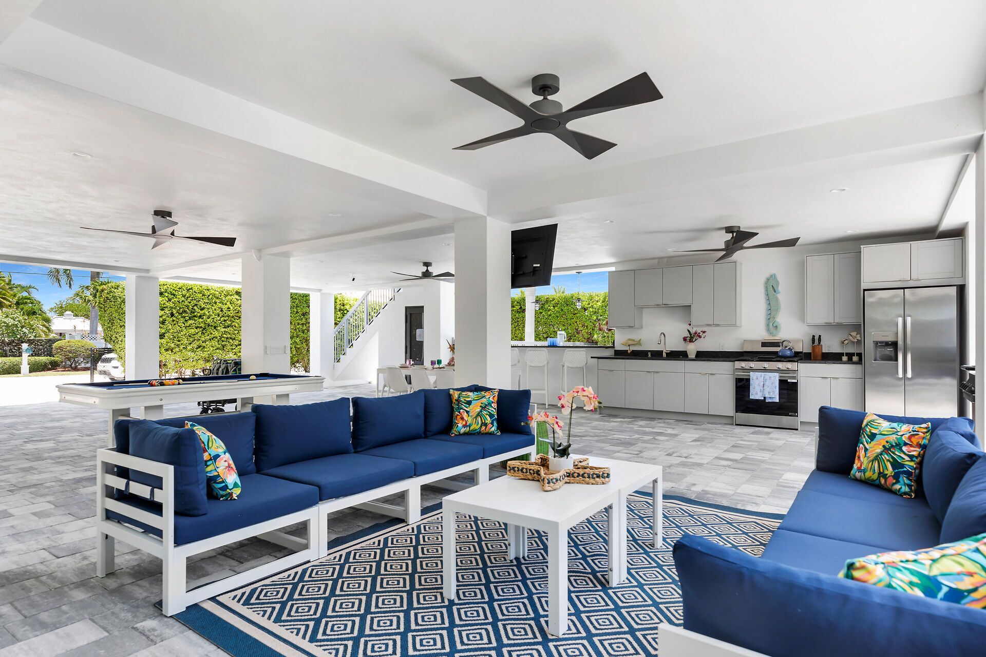 A modern open-plan living area with a pool table, blue sofas, and a kitchen with white cabinets.