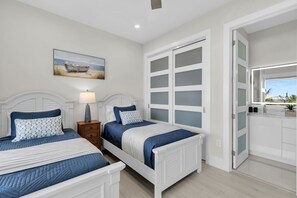 A bedroom with two beds, a nightstand, a lamp, a painting, and a bathroom visible through an open door. - Brand new, walking distance to Sombrero Beach! 4 Bed/4.5 Bath outdoor kitchen. (Marathon)