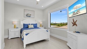 A bedroom with a bed, nightstands, a ceiling fan, a window with a view, and a starfish decoration. - Brand new, walking distance to Sombrero Beach! 4 Bed/4.5 Bath outdoor kitchen. (Marathon)