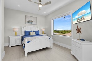 A bedroom with a bed, nightstands, a ceiling fan, a window with a view, and a starfish decoration. - Brand new, walking distance to Sombrero Beach! 4 Bed/4.5 Bath outdoor kitchen. (Marathon)