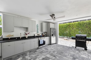 A modern kitchen with grey cabinets, a stainless steel refrigerator, a gas stove, and a ceiling fan. - Brand new, walking distance to Sombrero Beach! 4 Bed/4.5 Bath outdoor kitchen. (Marathon)