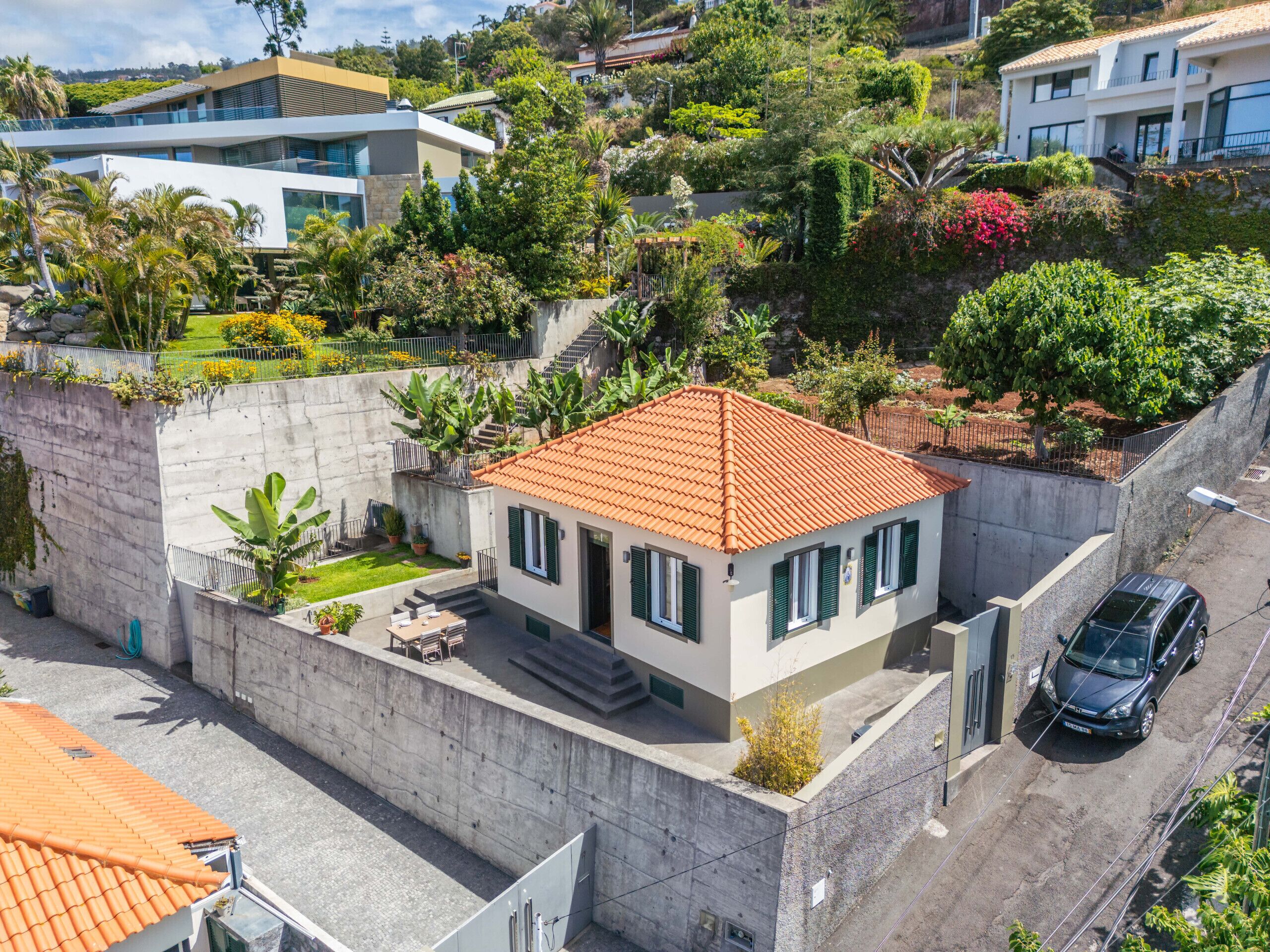 A modern two-story house with a red-tiled roof, a small front yard, and a car parked in the driveway.
