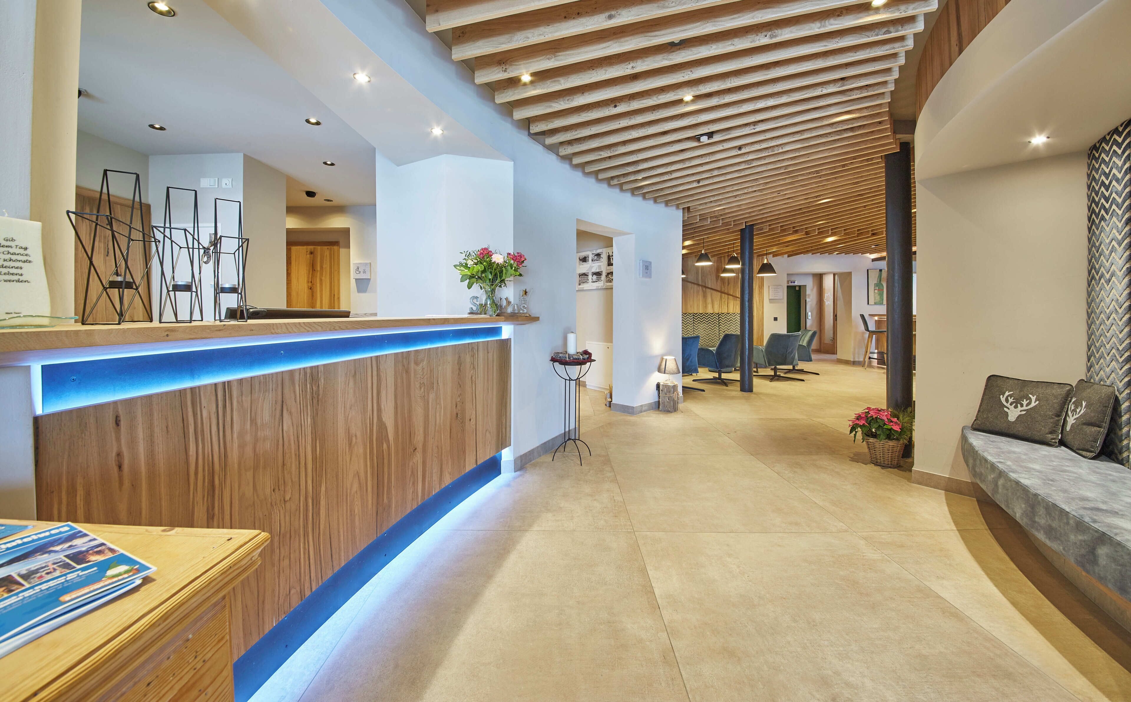 Zona de recepción con un mostrador de madera, una barra iluminada en azul y un área de estar con un sofá y sillas.