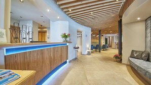 Zona de recepción con un mostrador de madera, una barra iluminada en azul y un área de estar con un sofá y sillas.
