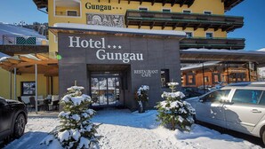 Hotel Gungau, con restaurante cafetería, suelo cubierto de nieve y un coche estacionado frente a él.