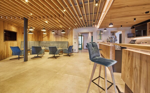A modern interior with wooden ceiling beams, bar area, seating with stools, and a counter with a coffee machine.